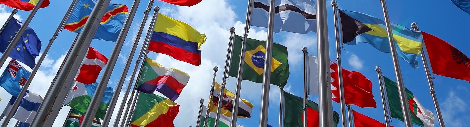 Looking up at flags of the world against a clear blue sky.